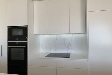Inredning av ett modernt litet vit vitt kök, med vita skåp, vitt stänkskydd och en köksö