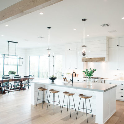 Large transitional u-shaped light wood floor and brown floor open concept kitchen photo in Austin with a farmhouse sink, shaker cabinets, white cabinets, quartzite countertops, white backsplash, stone slab backsplash, stainless steel appliances, an island and gray countertops