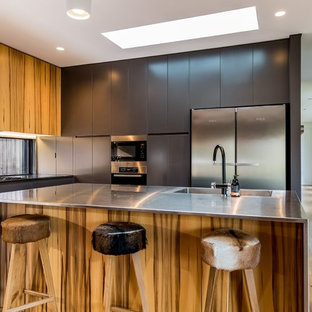 Contemporary l-shaped kitchen in Wollongong with an integrated sink, flat-panel cabinets, grey cabinets, stainless steel benchtops, stainless steel appliances, medium hardwood floors, with island and brown floor.