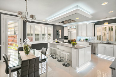 Eat-in kitchen - large transitional l-shaped porcelain tile and white floor eat-in kitchen idea in Seattle with an undermount sink, raised-panel cabinets, white cabinets, white backsplash, stainless steel appliances, an island and gray countertops
