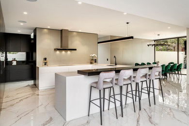 Large trendy u-shaped marble floor and white floor eat-in kitchen photo in Melbourne with an undermount sink, white cabinets, marble countertops, beige backsplash, porcelain backsplash, black appliances, no island and white countertops