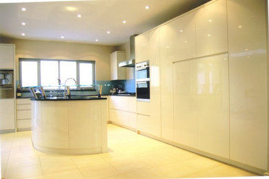 Large contemporary l-shaped open plan kitchen in London with a built-in sink, flat-panel cabinets, grey cabinets, granite worktops, black splashback, glass sheet splashback, stainless steel appliances, ceramic flooring and an island.