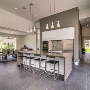 Mid-sized modern eat-in kitchen inspiration - Mid-sized minimalist single-wall travertine floor eat-in kitchen photo in Nashville with a single-bowl sink, flat-panel cabinets, white cabinets, solid surface countertops, mosaic tile backsplash, stainless steel appliances and an island