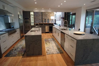 Example of a huge minimalist galley orange floor open concept kitchen design in Dallas with an undermount sink, flat-panel cabinets, white cabinets, granite countertops, gray backsplash, stainless steel appliances, two islands and gray countertops