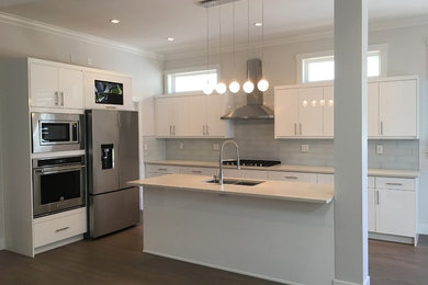 Example of a mid-sized minimalist l-shaped laminate floor and brown floor eat-in kitchen design in Vancouver with a double-bowl sink, flat-panel cabinets, white cabinets, quartz countertops, gray backsplash, ceramic backsplash, stainless steel appliances, an island and white countertops