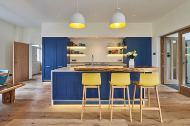 Design ideas for a large contemporary single-wall open plan kitchen in Other with a built-in sink, shaker cabinets, blue cabinets, quartz worktops, grey splashback, stone tiled splashback, white appliances, medium hardwood flooring, an island, brown floors and grey worktops.