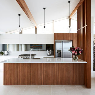 Photo of a mid-sized contemporary galley open plan kitchen in Sydney with a double-bowl sink, flat-panel cabinets, white cabinets, quartz benchtops, grey splashback, mirror splashback, stainless steel appliances, ceramic floors, with island, grey floor and white benchtop.