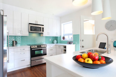 Example of a mid-sized trendy u-shaped medium tone wood floor eat-in kitchen design in Toronto with a double-bowl sink, flat-panel cabinets, white cabinets, solid surface countertops, blue backsplash, glass tile backsplash, stainless steel appliances and an island