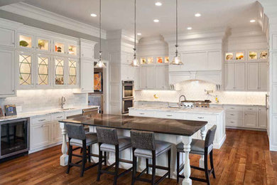 Photo of a large contemporary u-shaped kitchen/diner in Cincinnati with a submerged sink, shaker cabinets, white cabinets, white splashback, metro tiled splashback, integrated appliances, dark hardwood flooring, multiple islands and brown floors.