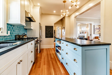 Inspiration for a large contemporary l-shaped medium tone wood floor and brown floor enclosed kitchen remodel in Vancouver with an undermount sink, shaker cabinets, white cabinets, granite countertops, blue backsplash, subway tile backsplash, stainless steel appliances, an island and black countertops