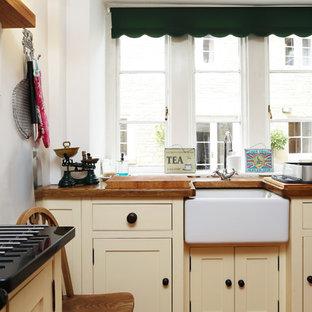 Photo of a small classic l-shaped kitchen/diner in London with a belfast sink, raised-panel cabinets, wood worktops, no island, brown worktops and beige cabinets.