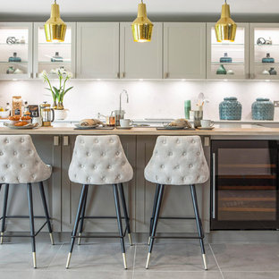 Medium sized classic l-shaped kitchen in Surrey with grey cabinets, white splashback, stainless steel appliances, an island, grey floors, glass-front cabinets, wood worktops and beige worktops.