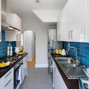 Ejemplo de cocina de galera, moderna, pequeña, cerrada, sin isla, con fregadero de doble seno, armarios con paneles lisos, puertas de armario blancas, encimera de madera, salpicadero azul, salpicadero de azulejos de cerámica, electrodomésticos de acero inoxidable y suelo de baldosas de porcelana