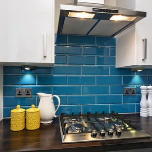 Small contemporary galley separate kitchen in London with an integrated sink, flat-panel cabinets, white cabinets, wood benchtops, blue splashback, ceramic splashback, stainless steel appliances, ceramic floors and no island.