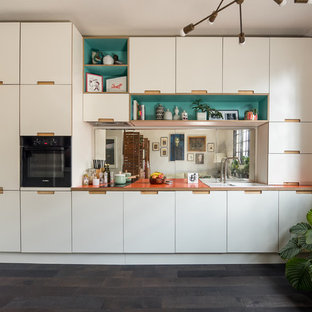 Design ideas for a small eclectic single-wall open plan kitchen in London with flat-panel cabinets, white cabinets, laminate benchtops, mirror splashback, dark hardwood floors, no island, a drop-in sink, black appliances, black floor and orange benchtop.
