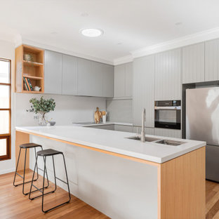 This is an example of a contemporary u-shaped kitchen in Adelaide with an undermount sink, flat-panel cabinets, grey cabinets, white splashback, stainless steel appliances, medium hardwood floors, a peninsula, brown floor and white benchtop.