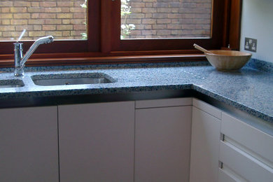 Photo of a medium sized modern l-shaped kitchen in London with recycled glass countertops, blue splashback, an island and blue worktops.