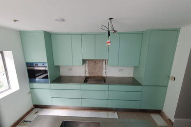 Modelo de cocina lineal moderna abierta con fregadero integrado, armarios con paneles lisos, puertas de armario verdes, encimera de acero inoxidable y una isla