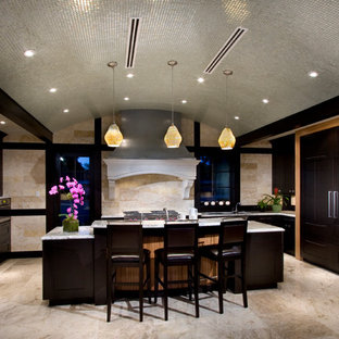 Diseño de cocina de galera, contemporánea, de tamaño medio, cerrada, con armarios estilo shaker, puertas de armario marrones, encimera de mármol, salpicadero beige, salpicadero de travertino, electrodomésticos de acero inoxidable y una isla