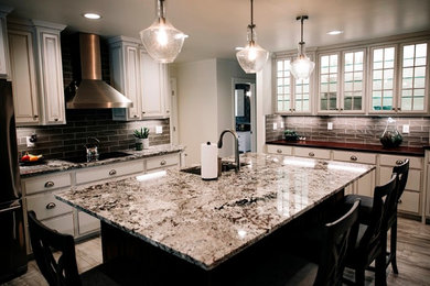 Example of a large classic u-shaped medium tone wood floor and brown floor enclosed kitchen design in Other with a drop-in sink, raised-panel cabinets, white cabinets, granite countertops, gray backsplash, subway tile backsplash, stainless steel appliances and an island
