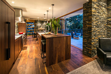 This is an example of a medium sized modern single-wall kitchen/diner in Atlanta with flat-panel cabinets, medium wood cabinets, wood worktops, multi-coloured splashback, stone tiled splashback, integrated appliances, medium hardwood flooring, multiple islands, a submerged sink and brown floors.