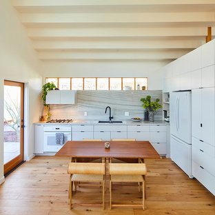 Ispirazione per una cucina contemporanea con lavello sottopiano, ante lisce, ante bianche, paraspruzzi bianco, elettrodomestici bianchi, pavimento in legno massello medio, nessuna isola, pavimento marrone e top bianco