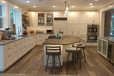 Design ideas for a large traditional l-shaped open plan kitchen in Seattle with a submerged sink, shaker cabinets, white cabinets, engineered stone countertops, white splashback, metro tiled splashback, integrated appliances, medium hardwood flooring, an island and brown floors.
