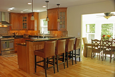Exempel på ett stort klassiskt kök, med stänkskydd i stenkakel, rostfria vitvaror, mellanmörkt trägolv, en undermonterad diskho, luckor med infälld panel, skåp i mellenmörkt trä, granitbänkskiva, brunt stänkskydd och en halv köksö