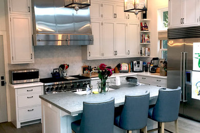 Klassische Küche mit Landhausspüle, Schrankfronten mit vertiefter Füllung, weißen Schränken, Granit-Arbeitsplatte, Küchengeräten aus Edelstahl, braunem Holzboden und Kücheninsel in Los Angeles