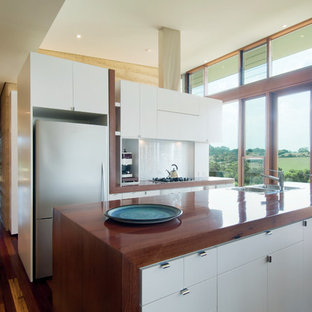 Inspiration for an expansive modern galley open plan kitchen in Melbourne with a drop-in sink, flat-panel cabinets, stainless steel appliances, wood benchtops, white cabinets, white splashback, glass sheet splashback, dark hardwood floors and with island.