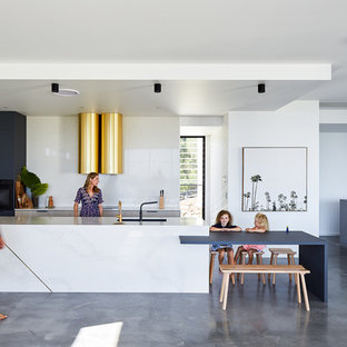 This is an example of a modern galley open plan kitchen in Gold Coast - Tweed with an undermount sink, flat-panel cabinets, light wood cabinets, white splashback, black appliances, concrete floors, with island, grey floor and white benchtop.