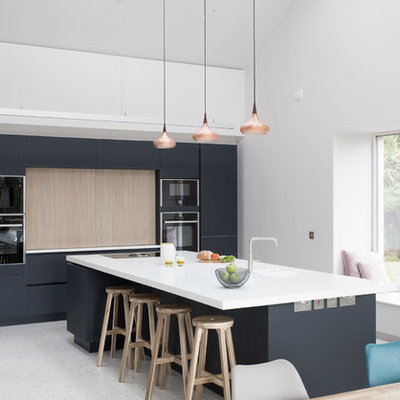 Kitchen - large contemporary single-wall concrete floor and gray floor kitchen idea in Other with an integrated sink, solid surface countertops, black appliances, an island, flat-panel cabinets and black backsplash