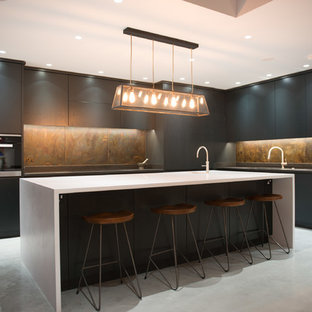 This is an example of an expansive modern l-shaped open plan kitchen in London with a drop-in sink, flat-panel cabinets, dark wood cabinets, quartzite benchtops, multi-coloured splashback, metal splashback, stainless steel appliances, concrete floors, with island, grey floor and white benchtop.
