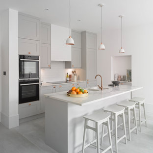 Design ideas for a scandinavian kitchen in London with a double-bowl sink, shaker cabinets, grey cabinets, white splashback, black appliances, with island, grey floor and white benchtop.