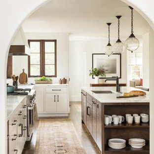 Ispirazione per una cucina mediterranea con lavello sottopiano, ante lisce, ante bianche, paraspruzzi bianco, elettrodomestici in acciaio inossidabile, parquet scuro e pavimento marrone