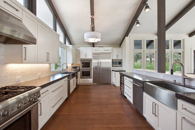 Inspiration for a mid-sized transitional l-shaped medium tone wood floor and brown floor open concept kitchen remodel in San Francisco with white cabinets, quartz countertops, a farmhouse sink, stainless steel appliances, recessed-panel cabinets, gray backsplash, stone tile backsplash and an island