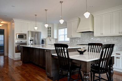 Eat-in kitchen - large transitional l-shaped medium tone wood floor and brown floor eat-in kitchen idea in Toronto with an undermount sink, shaker cabinets, white cabinets, quartzite countertops, gray backsplash, stone tile backsplash, stainless steel appliances and an island