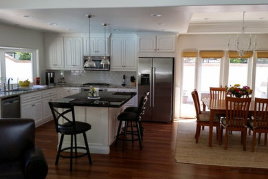 Mid-sized transitional u-shaped light wood floor eat-in kitchen photo in San Francisco with an undermount sink, shaker cabinets, white cabinets, glass countertops, white backsplash, ceramic backsplash, white appliances and an island