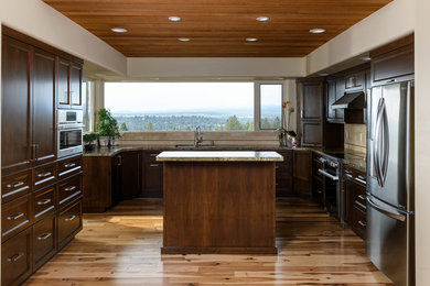 Large elegant u-shaped light wood floor and brown floor enclosed kitchen photo in Other with a double-bowl sink, recessed-panel cabinets, dark wood cabinets, granite countertops, beige backsplash, travertine backsplash, stainless steel appliances and an island