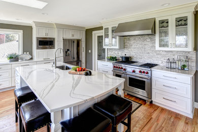 Example of a large transitional l-shaped light wood floor open concept kitchen design in Portland with a single-bowl sink, shaker cabinets, white cabinets, quartz countertops, gray backsplash, ceramic backsplash, stainless steel appliances and an island