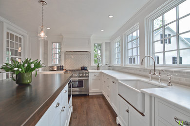 Inspiration for a large timeless u-shaped dark wood floor and brown floor enclosed kitchen remodel in Boston with a farmhouse sink, recessed-panel cabinets, white cabinets, quartzite countertops, beige backsplash, subway tile backsplash, paneled appliances and an island