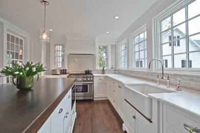 Large traditional u-shaped enclosed kitchen in Boston with a belfast sink, recessed-panel cabinets, white cabinets, quartz worktops, beige splashback, metro tiled splashback, integrated appliances, dark hardwood flooring, an island and brown floors.