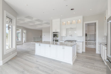 Example of a mid-sized trendy u-shaped vinyl floor and beige floor eat-in kitchen design in Other with an undermount sink, recessed-panel cabinets, white cabinets, granite countertops, white backsplash, subway tile backsplash, stainless steel appliances, an island and multicolored countertops