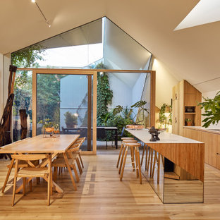 This is an example of a small contemporary galley open plan kitchen in Melbourne with laminate benchtops, white splashback, ceramic splashback, black appliances, medium hardwood floors, with island, brown floor, white benchtop, flat-panel cabinets and medium wood cabinets.