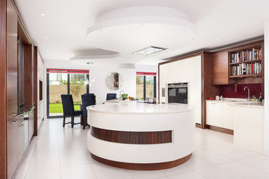 This is an example of an expansive contemporary open plan kitchen in Other with a built-in sink, flat-panel cabinets, medium wood cabinets, composite countertops, red splashback, glass sheet splashback, black appliances and an island.
