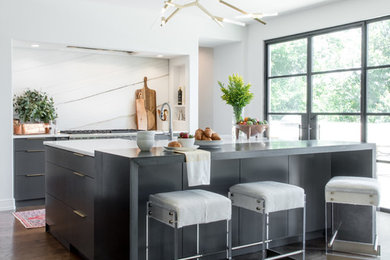 Inspiration for a large transitional l-shaped medium tone wood floor and brown floor open concept kitchen remodel in Other with a farmhouse sink, flat-panel cabinets, gray cabinets, marble countertops, white backsplash, marble backsplash, stainless steel appliances, an island and white countertops