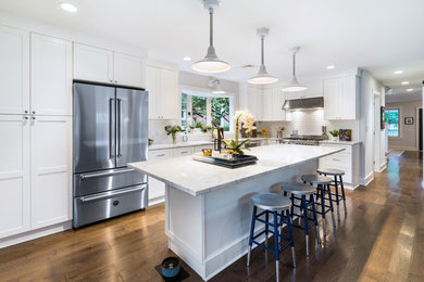 Example of a mid-sized transitional l-shaped dark wood floor and brown floor kitchen design in Philadelphia with an undermount sink, shaker cabinets, white backsplash, stainless steel appliances, an island, white countertops and white cabinets