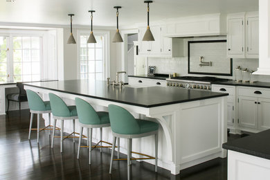 Example of a beach style dark wood floor and brown floor kitchen design in New York with a farmhouse sink, shaker cabinets, white cabinets, multicolored backsplash, stainless steel appliances and an island