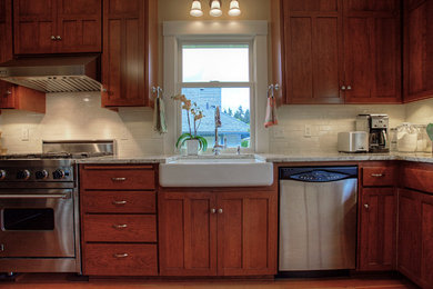 Example of a mid-sized arts and crafts l-shaped medium tone wood floor enclosed kitchen design in Seattle with a farmhouse sink, shaker cabinets, medium tone wood cabinets, granite countertops, white backsplash, subway tile backsplash, stainless steel appliances and no island