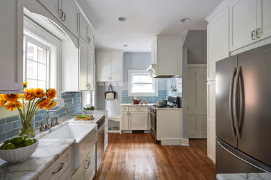 Example of a mid-sized cottage medium tone wood floor and brown floor enclosed kitchen design in Other with a farmhouse sink, shaker cabinets, white cabinets, marble countertops, blue backsplash, subway tile backsplash, stainless steel appliances and no island